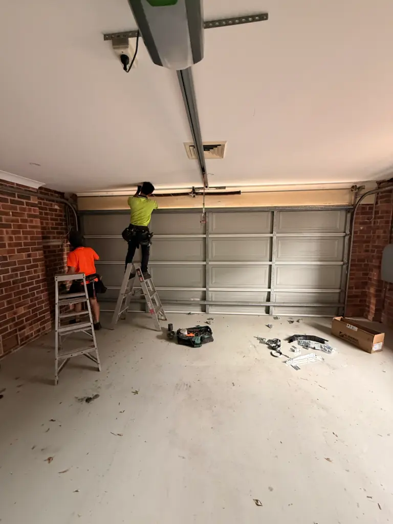 Two Gold Garage Door technicians installing a sectional garage door in a Sydney garage