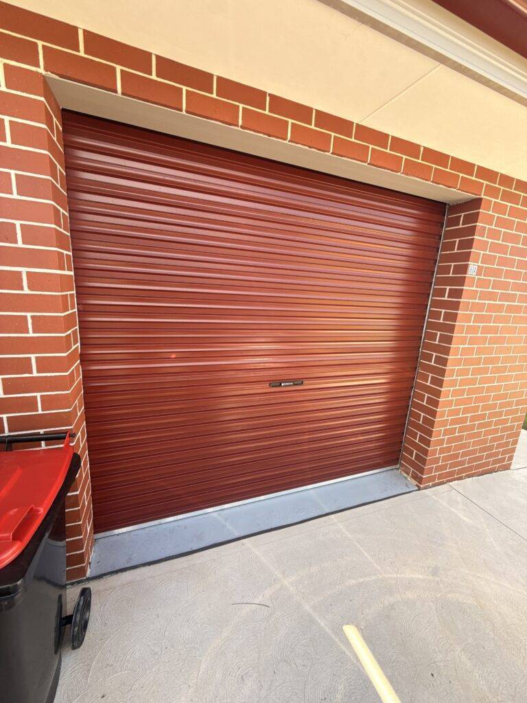 Red roller garage door installed in a brick garage